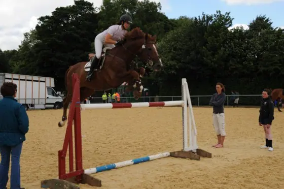 A bay jumping a red and white upright as people watch
